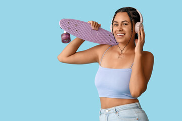 Wall Mural - Young African-American woman with skateboard listening to music on blue background