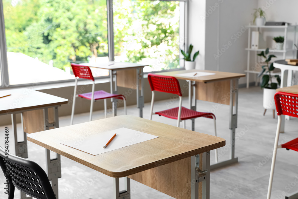 Sheet of paper and pencil on desk in empty classroom. Closeup