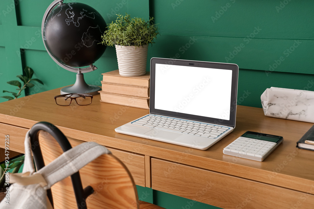 Workspace with school supplies and laptop near green wall