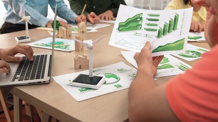 Wall Mural - Excellent business team discuss on eco house project at messy table with green energy using graph with windmill, home, tree model for decreasing carbon usage to save earth. Focus on hand. Delineation.