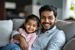 © gfx_yasir - A man and a little girl are sitting on a couch, smiling. The man is holding the girl