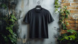 © Bartek - Black Blank T-Shirt Hanging on Textured Wall with Greenery Background for Design Mockup, Fashion Display, and Graphic Template
