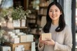 © Tapanut - Smiling woman holding a soap bar in front of a storefront with various natural products displayed in the background.