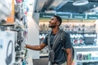 © unai - Young african man in a tech store looking at headphones