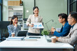 © Phushutter - In a boardroom, an Asian team meets at a desk, presenting financial terms and strategies. Executives and employees collaborate, sharing ideas and work guidelines for success during an annual meeting.