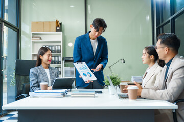 In a boardroom, an Asian team meets at a desk, presenting financial terms and strategies. Executives and employees collaborate, sharing ideas and work guidelines for success during an annual meeting.