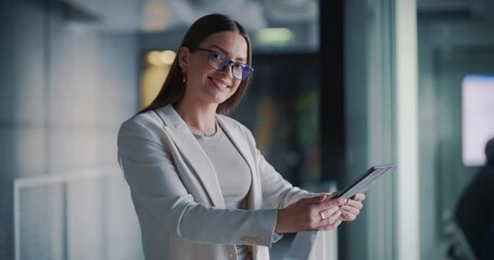 Poster - Successful Businesswoman in a Stylish Outfit Holding a Tablet Computer, Standing in Modern Office Setting, Posing and Looking at Camera with a Smile. Portrait of a Beautiful Caucasian Manager