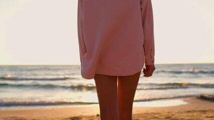 Wall Mural - young girl in a pink shirt walks along the beach at sunset. sunset on the beach. girl having fun on the beach. summer mood.