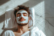 © 7707601 - Unshaven man having cosmetic mask is lying on the tiles. Anti-aging, relax, men's self-care, hygiene.
