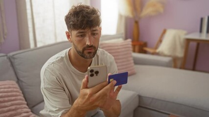 Wall Mural - Young man using smartphone with credit card in living room home interior