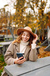 © maxbelchenko - A young woman enjoying a peaceful autumn day outdoors, sitting at a table with her phone surrounded by colorful leaves