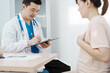 © NanSan - Asian female doctor listens to belly of pregnant mother during a prenatal exam in clinic. doctor provides caring advice, ensuring the health and happiness of the expecting mother and baby.
