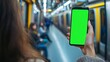 © Lumos Maxima - Woman is holding a smartphone with green or chroma key screen in blurred subway train station blurred background, perfect for showcasing apps and mobile technology, travel and navigation concept