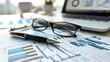 © liliyabatyrova - A workspace features detailed business documents with financial graphs, a stylish pen, and stylish glasses. A laptop displays various analytics, creating a professional atmosphere
