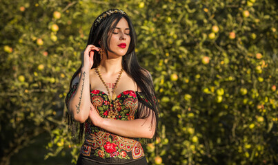 Black hair woman in dark clothes on a nature background, corset with ethnic prints, Slavic style 