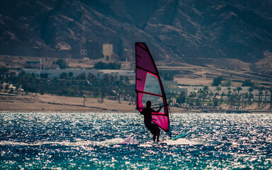 Poster - silhouette of a surfer in the Red Sea on the background of a rocky coast with palm trees and a hotel in Egypt Dahab