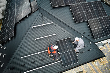 Wall Mural - Installers building photovoltaic solar module station on roof of house. Men electricians in helmets installing solar panel system outdoors. Concept of alternative and renewable energy. Aerial view.