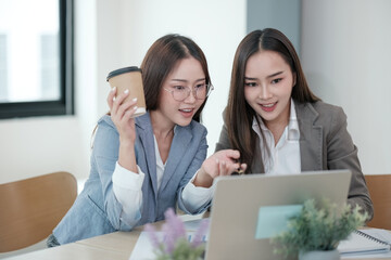 Wall Mural - Two women are sitting at a table with a laptop in front of them