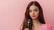 © Iswanto - Young woman with long brown hair, wearing a pink dress, holds a makeup brush in her hand, looking at the camera with a gentle smile.