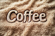 © sergign - The word 'Coffee' displayed in bold, plush lettering on a soft, beige, textured fabric background, emphasizing warmth and richness.