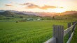 © nunoi - Captivating sunset over a serene green pasture, framed by a rustic wooden fence and majestic mountain silhouettes in the background.
