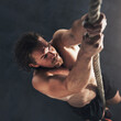 © peopleimages.com - Man, bodybuilder and climb rope for fitness at gym for bodybuilding with strength and determination. Male person, muscles and strong with top of training, workout and exercise for health or self care