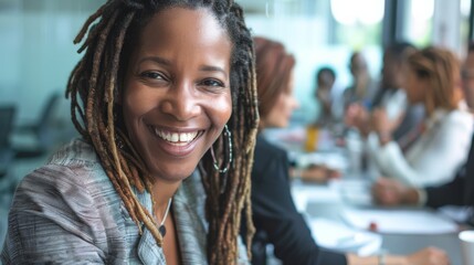 Sticker - A woman with dreadlocks beams a bright smile while sitting at a table in a modern office setting, exuding confidence and warmth.