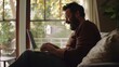 © VK Studio - A man sits comfortably on a couch, deeply absorbed in his laptop, bathed in natural light from large windows, exuding focus and contentment.