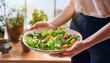 © Kseniia - a plate with a salad of herbs and vegetables in hands against the background of a kitchen with beautiful light