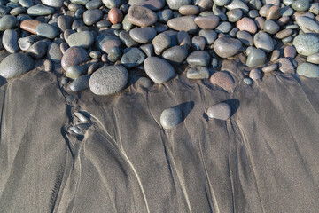 Variety of different pebbles and water marks on a black volcanic beach in Playa El Tunco, El Salvador. Abstract background texture with sandy pattern and contrasting natural hard and soft textures.