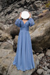 © Milou Dirks - portrait of woman in classic blue dress holding round mirror in front of face standing near lava cliff on beach in Madeira