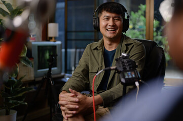 Wall Mural - Two hosts of podcasts a happy radio host in a chic studio, one speaking into the microphone as the other listens intently while donning headphones to record a podcast.