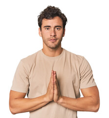 Wall Mural - Young Hispanic man in studio praying, showing devotion, religious person looking for divine inspiration.