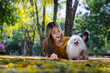 © kamonrat - Woman Lying on Blanket Reading with a Smiling Pomeranian Dog in a Scenic Park with Yellow Leaves and Green Trees