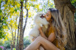 © kamonrat - Woman Sharing a Loving Kiss with Her Pomeranian in a Tranquil Park, Surrounded by Vibrant Nature and Sunshine