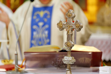 Wall Mural - Holy Cross with Jesus Christ on the altar during the Holy Mass, the priest in the background and empty space for text.