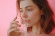 © Anastasia Knyazeva - Woman drinking water from a glass, highlighted against a soft pink background, promoting hydration and wellness.