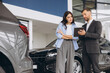 © anatoliycherkas - Young woman customer female buyer client wears shirt consult with salesman hold tablet choosing auto want to buy new automobile in car showroom vehicle salon dealership store motor show.