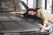 © anatoliycherkas - Charming young Caucasian woman hugging hood of new car in modern bright car dealership. Happy girl buyer rejoices after making her dream come true.