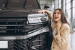 © anatoliycherkas - Charming young Caucasian woman hugging hood of new car and show fist and say yes in modern bright car dealership. Happy girl buyer rejoices after making her dream come true.