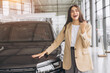 © anatoliycherkas - Charming young Caucasian woman hugging hood of new car and show fist and say yes in modern bright car dealership. Happy girl buyer rejoices after making her dream come true.