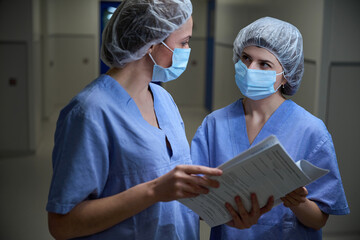 Female doctors in protective masks taking holding patient questionnaire. Medical service concept