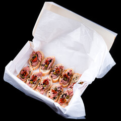 Canvas Print - Fresh bruschetta with meat, tomatoes, capers and sauce in a paper box.