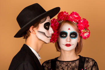 Couple with dark skull makeup on beige background. Halloween face art