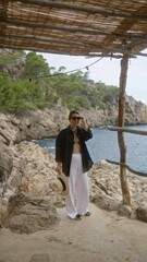 Poster - Young woman enjoying outdoors in cala deia, mallorca, posing near the sea under a bamboo shade structure.