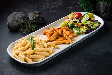 Canvas Print - Dinner Penne pasta with fried chicken and a green salad of olives, lettuce, arugula, cherry tomatoes, corn and carrots.