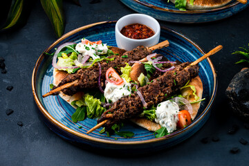 Sticker - Kebab, barbecued beef on a stick with tomatoes, lettuce, onion, arugula, sour cream, tortilla and red sauce on a plate.