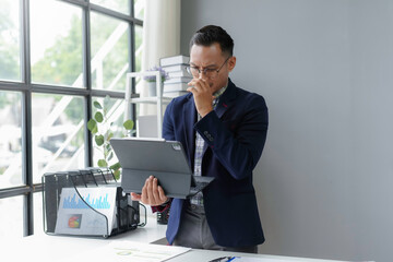 Wall Mural - Young businessman feeling stressed and frustrated while working on digital tablet with financial document on table at workplace