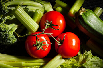 Wall Mural - tomato branch sliced celery sticks on black background