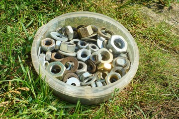 many different iron industrial different shiny mechanical for bolts round nuts lie in plastic box in green grass during daytime on street